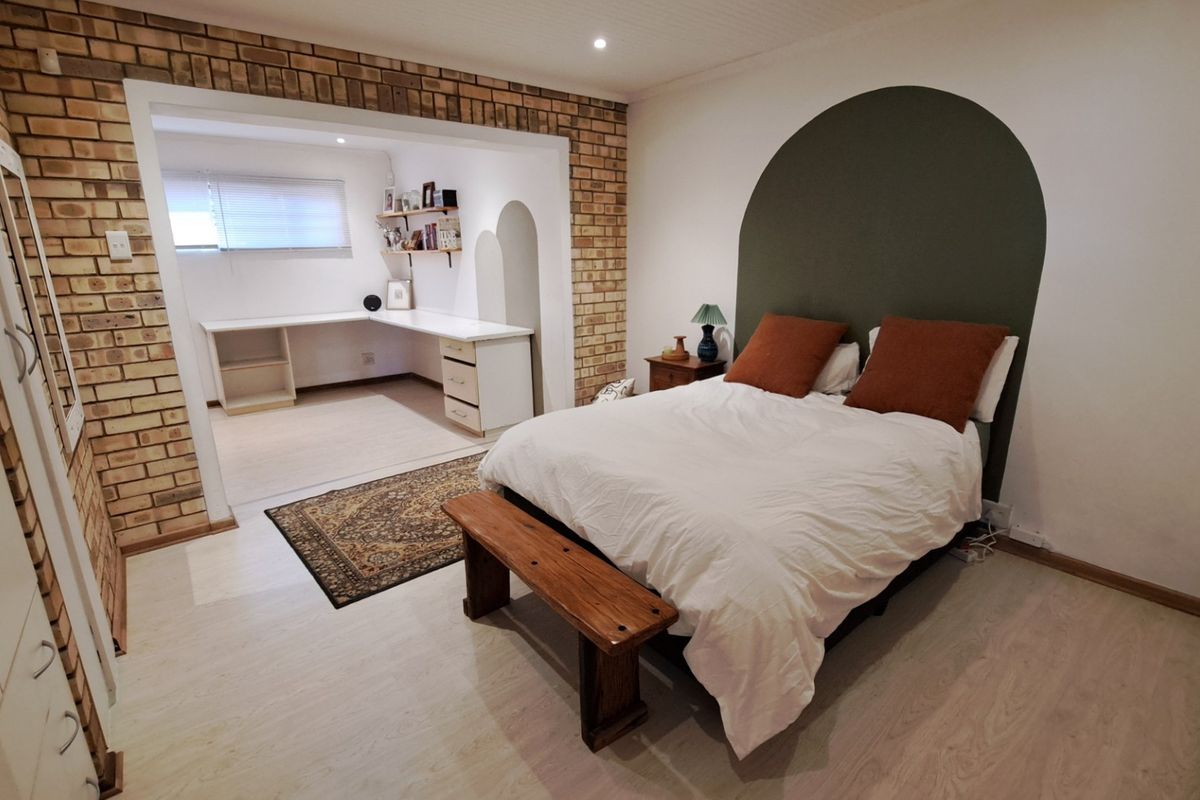 Spacious bedroom featuring an exposed brick wall, integrated study nook with built-in desk, and modern laminate flooring.