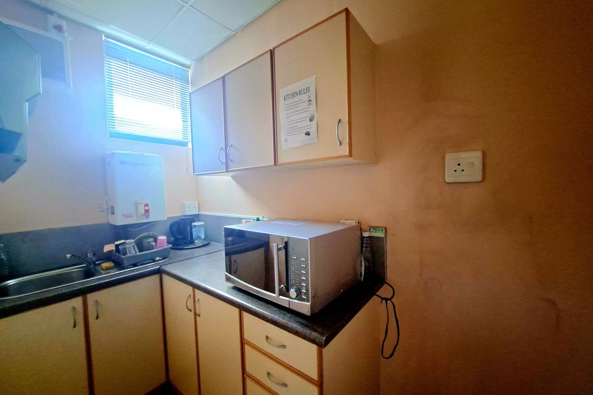 A compact office kitchenette featuring laminate cabinetry, a stainless steel sink, and a dedicated space for a microwave.
