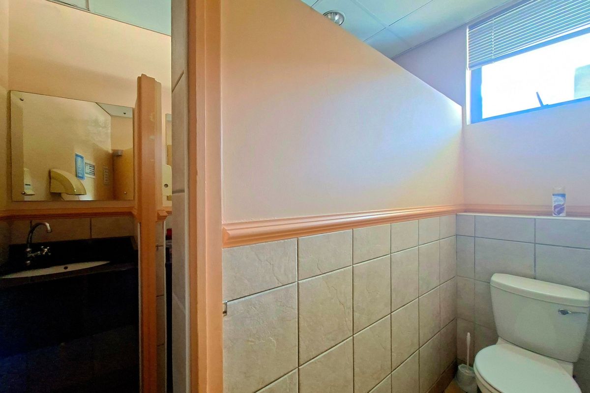 A functional office restroom featuring a partitioned toilet area and a separate vanity with a built-in sink and mirror.