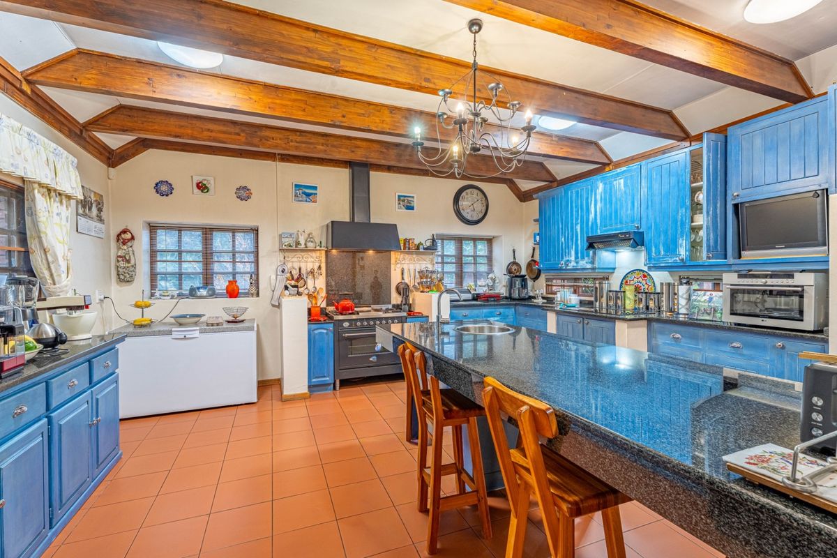 Spacious country-style kitchen featuring exposed timber beams, blue cabinetry, granite countertops, a central island, and a built-in oven with extractor fan.