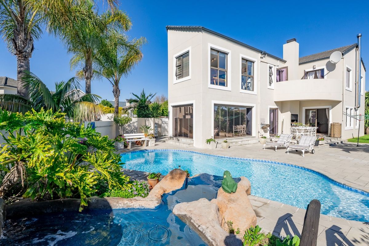 A spacious rear exterior view featuring a swimming pool, paved patio area, and a two-story residential building with a balcony.