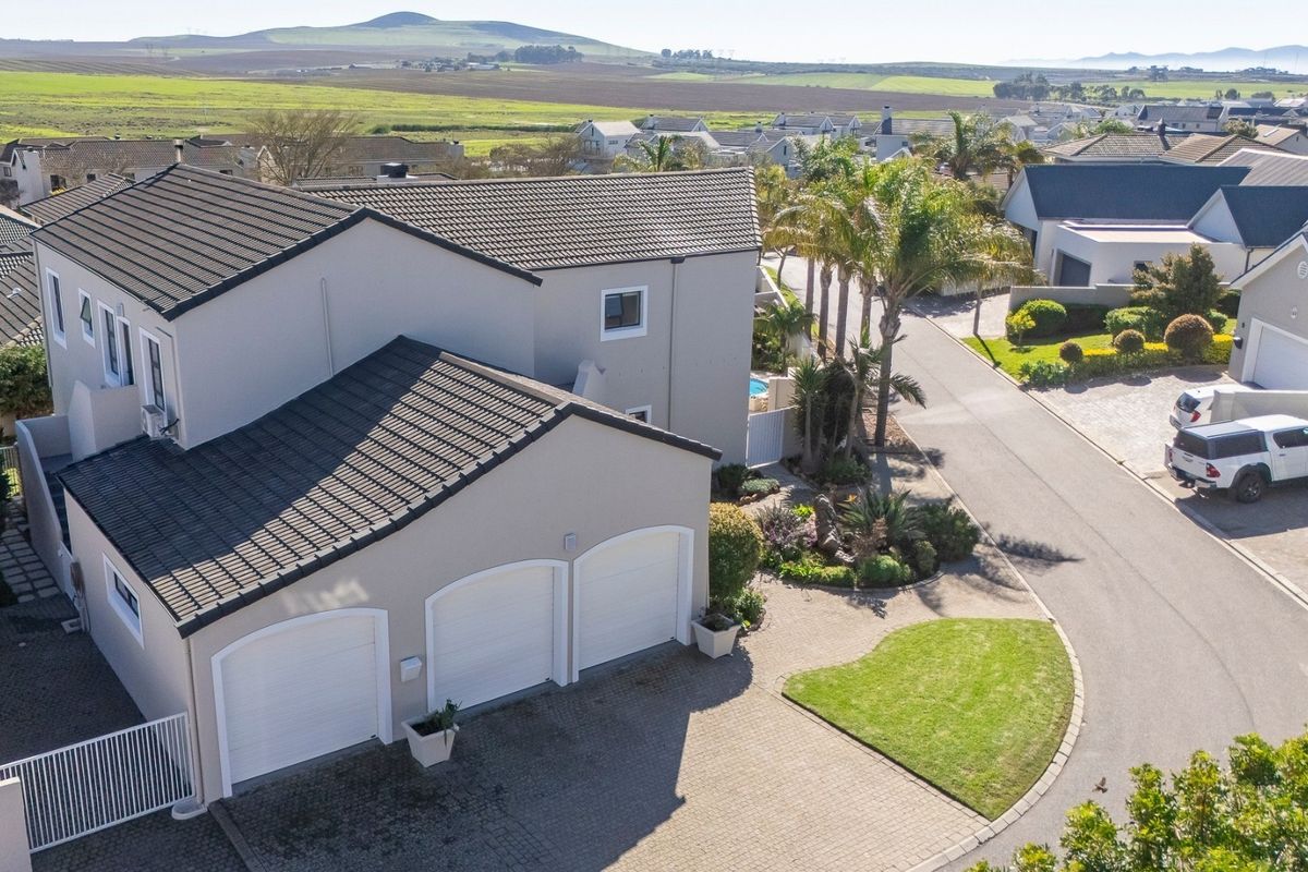 Aerial view of a modern residential property featuring a triple garage, paved driveway, and well-maintained exterior finishes in a quiet estate setting.