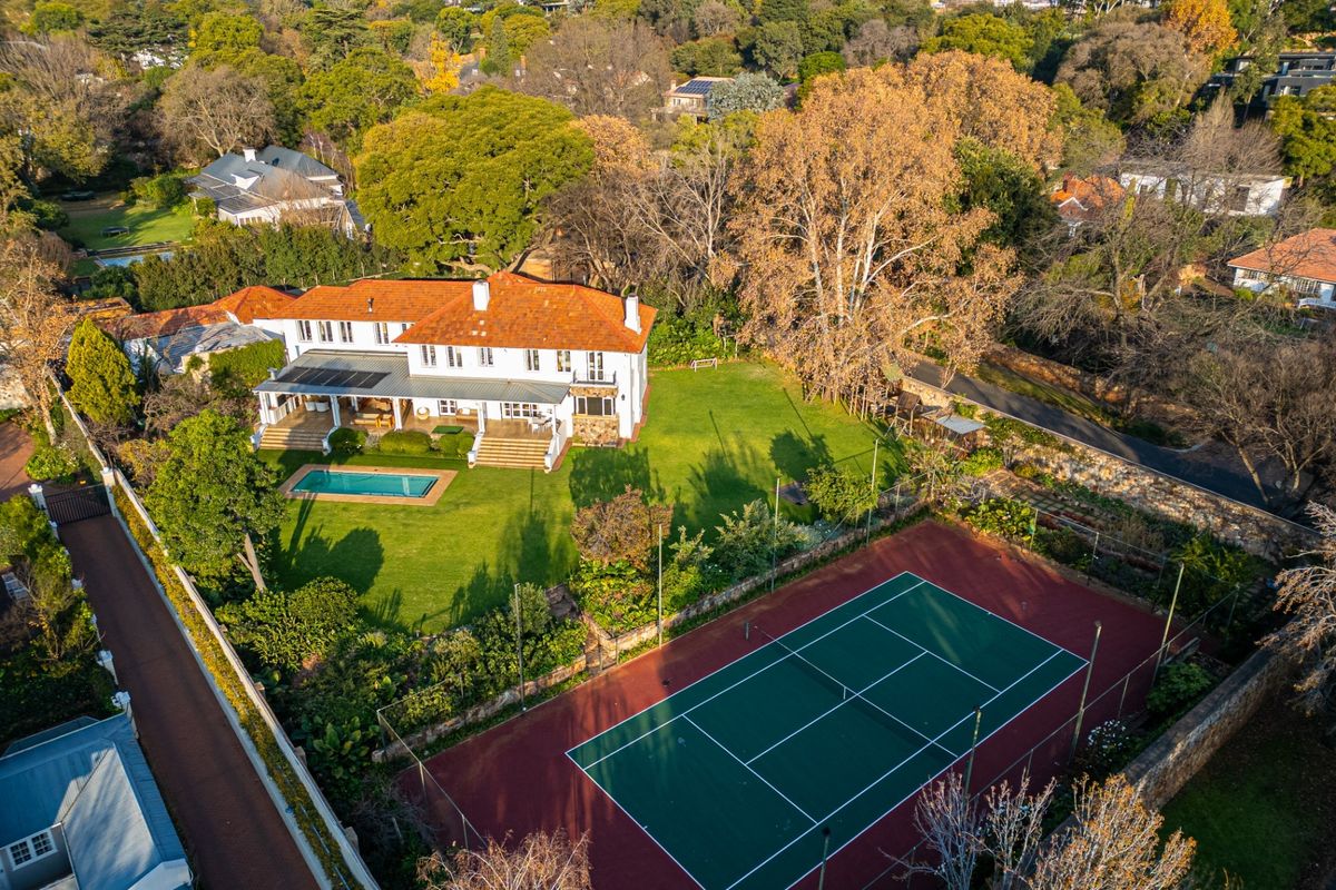 Aerial view of a large residential property featuring a swimming pool, tennis court, expansive garden, and a house with a terracotta tiled roof.