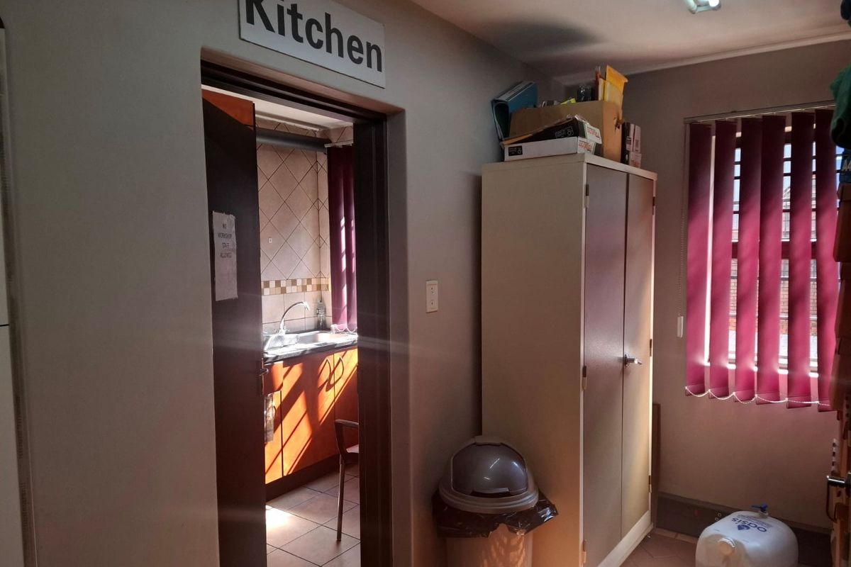 A view into a functional kitchen area featuring tiled splashbacks and a stainless steel sink, adjacent to a utility or office space.