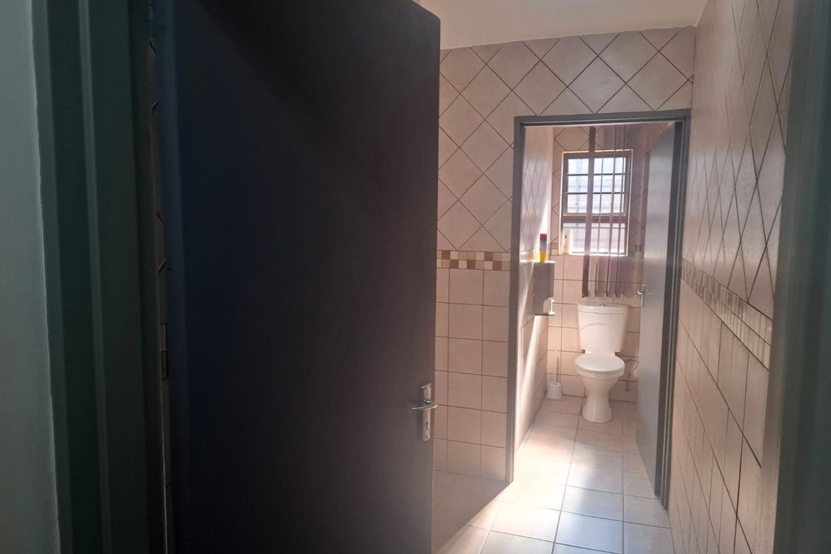 A functional bathroom featuring tiled walls and flooring, equipped with a standard toilet and natural light from a window.