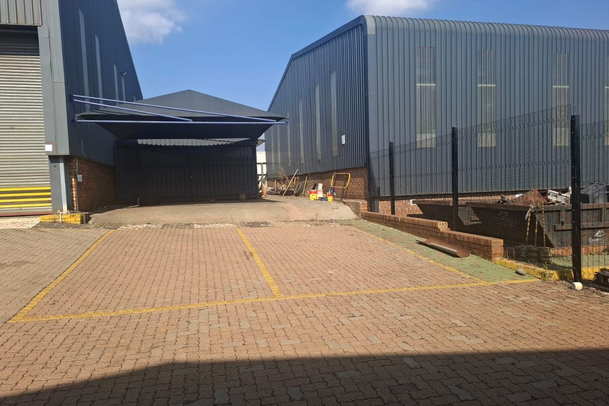 Industrial exterior view featuring paved parking area, metal cladding warehouse structures, and a covered loading or storage bay.