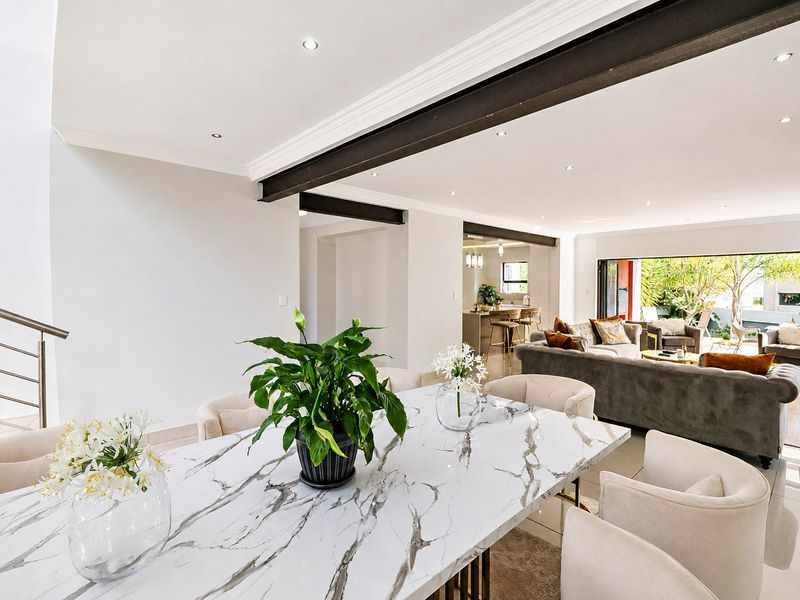 Spacious open-plan living and dining area featuring exposed steel beams, recessed lighting, and seamless flow to the outdoor patio through large sliding glass doors.