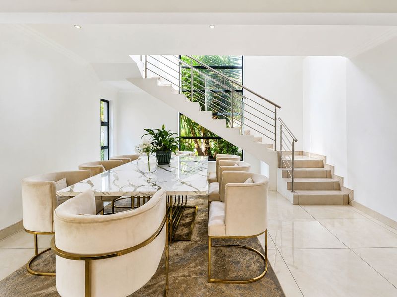 Elegant dining area featuring polished tiled floors, a modern staircase with stainless steel balustrades, and a large window overlooking the garden.