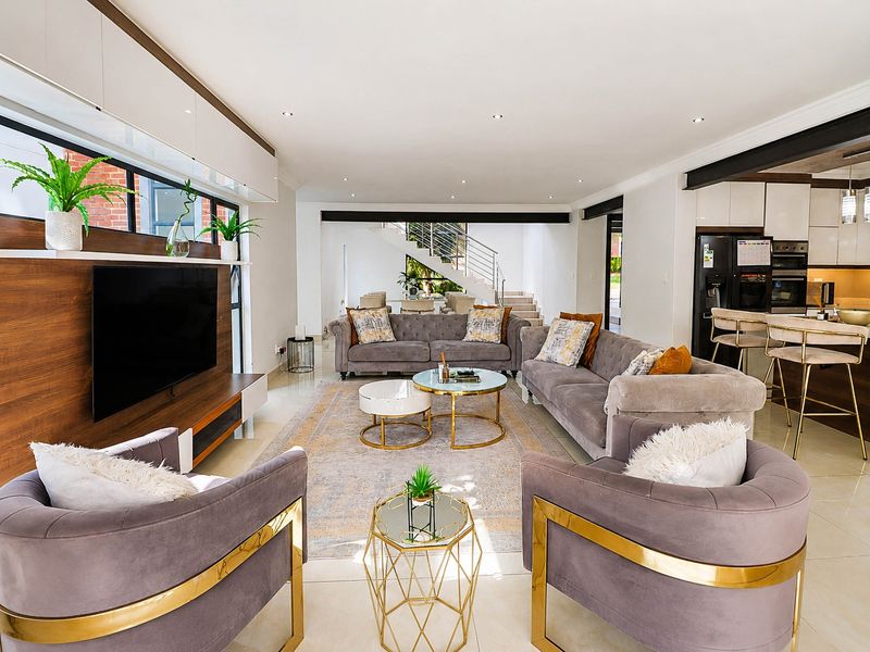 Spacious open-plan living area featuring a modern kitchen, built-in media unit, tiled floors, and a contemporary staircase with metal railings.