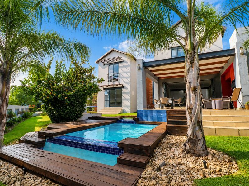 A well-maintained outdoor entertainment area featuring a swimming pool with timber decking, a covered patio, and a landscaped garden.