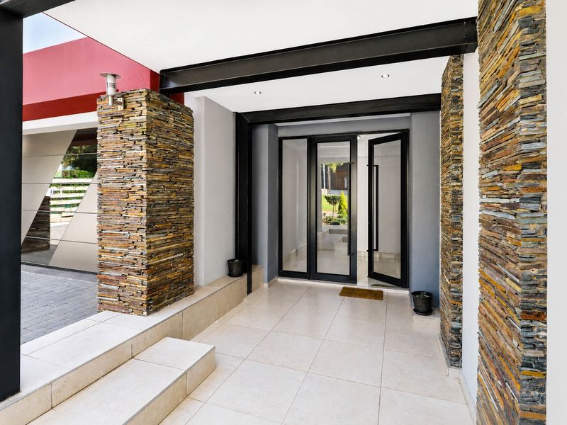 Modern entrance featuring stone-clad pillars, tiled flooring, and a sleek glass-panelled front door under a covered steel-framed portico.