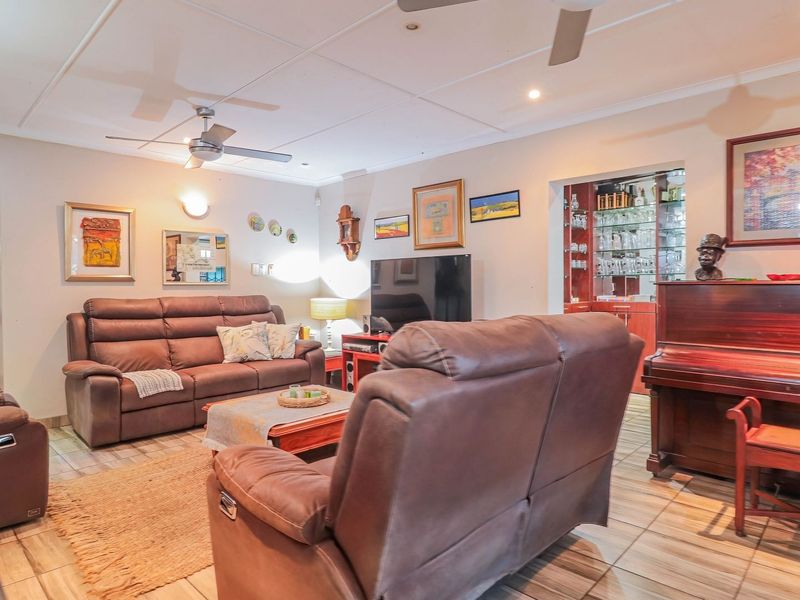 A comfortable living room featuring tiled flooring, a ceiling fan, and a built-in bar area with glass shelving.