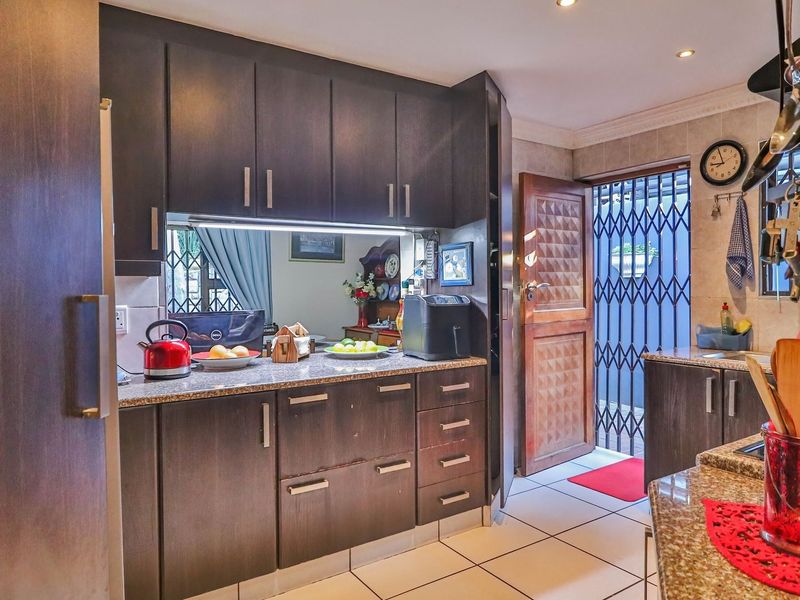 A functional kitchen featuring dark wood cabinetry, granite countertops, tiled flooring, and a security gate leading to the exterior.