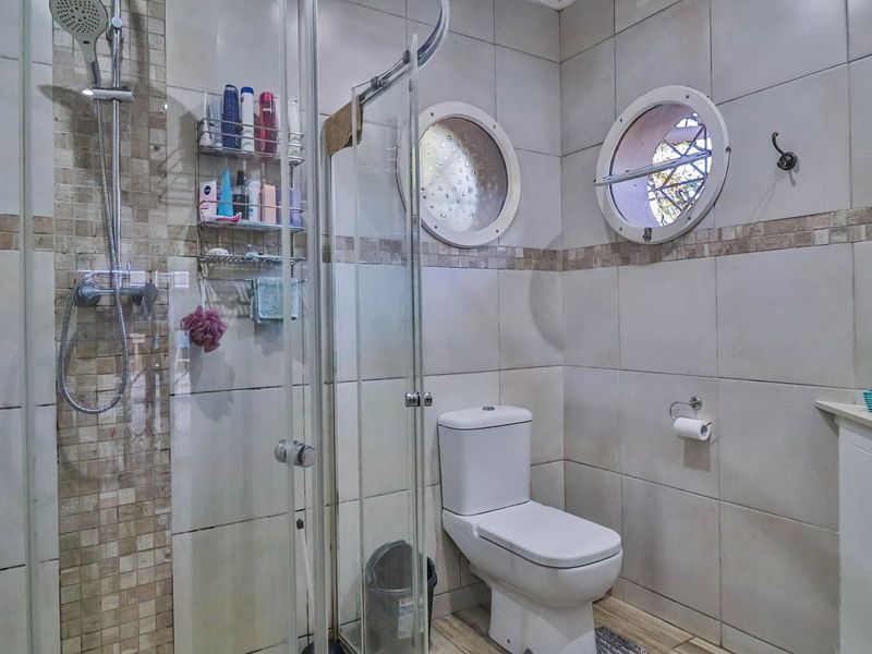 A functional bathroom featuring a glass-enclosed shower, modern toilet, and distinctive circular windows with tiled walls and flooring.