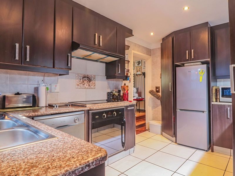 A functional kitchen featuring dark wood cabinetry, granite-look laminate countertops, a built-in oven with extractor fan, and tiled flooring.