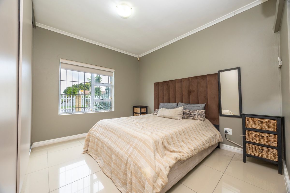 A well-maintained bedroom featuring neutral wall tones, tiled flooring, built-in wardrobe storage, and a window fitted with security bars.