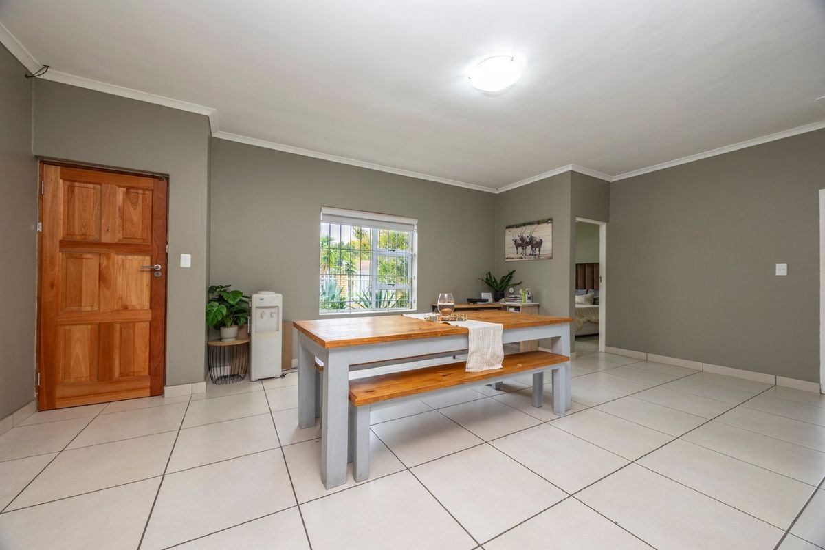 A spacious living area featuring neutral grey walls, large floor tiles, and a wooden entrance door with natural light from the window.
