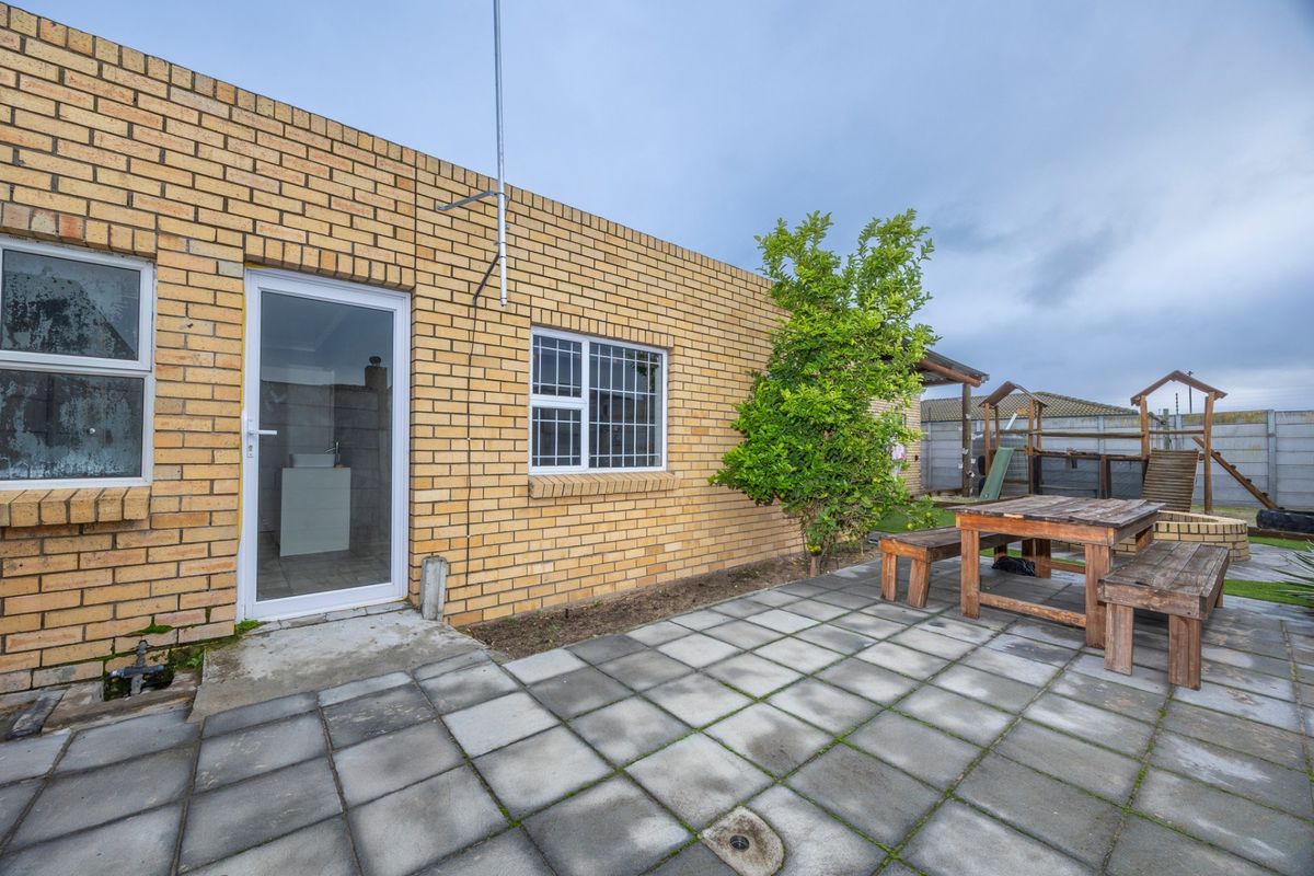 Rear exterior view of the property featuring a face brick facade, paved patio area, and aluminium window and door frames.