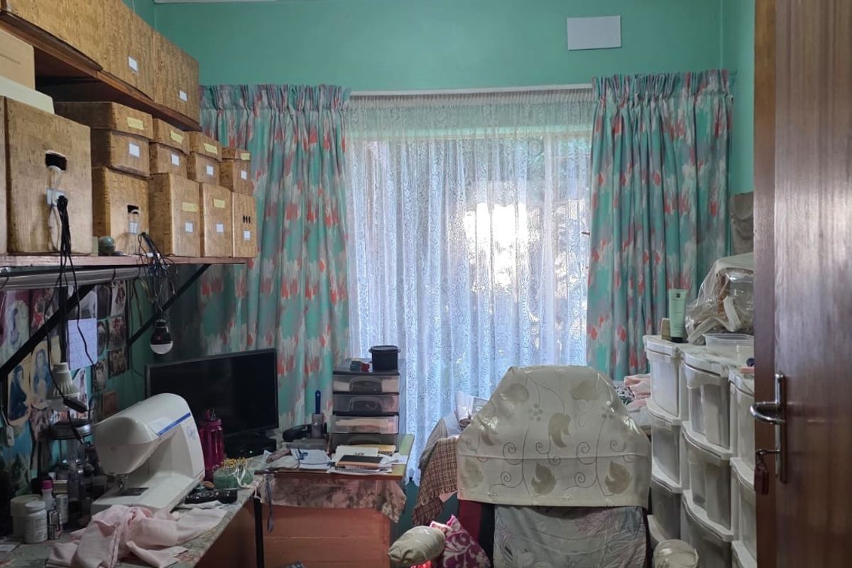 A multi-purpose room currently utilized as a workspace, featuring built-in shelving and a window with curtain treatments.