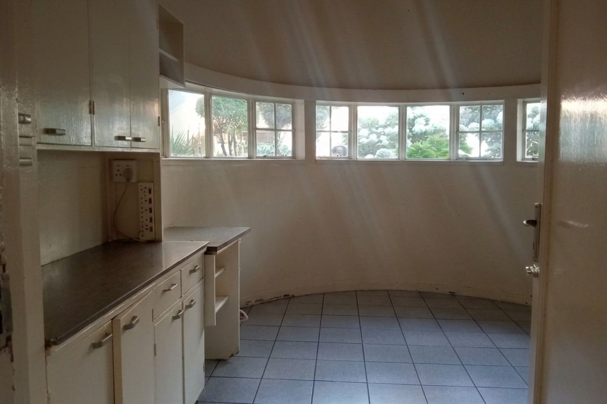A dated kitchen area featuring curved walls, tiled flooring, and original cabinetry, offering a unique layout with natural light from a series of windows.