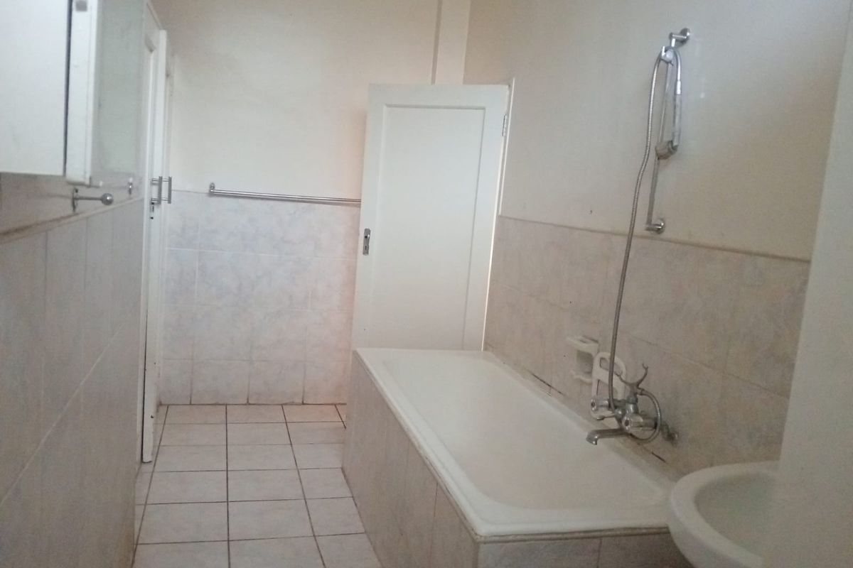 A functional bathroom featuring a built-in bathtub with a handheld shower fixture, tiled flooring, and wall-mounted towel rails.
