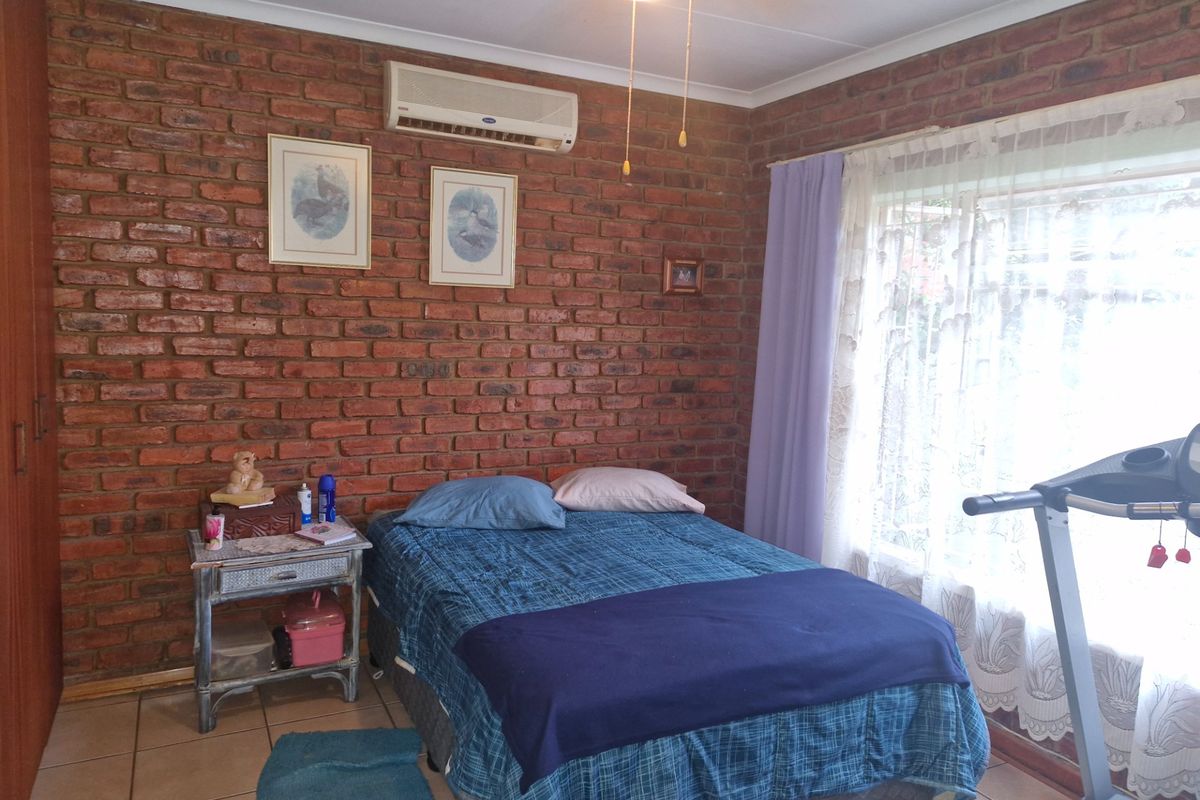 A bedroom featuring exposed brick walls, tiled flooring, and a wall-mounted air conditioning unit.