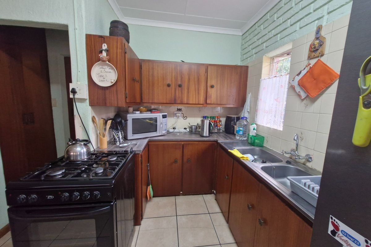 A functional kitchen featuring wooden cabinetry, a double basin sink, tiled flooring, and a built-in gas stove with oven.