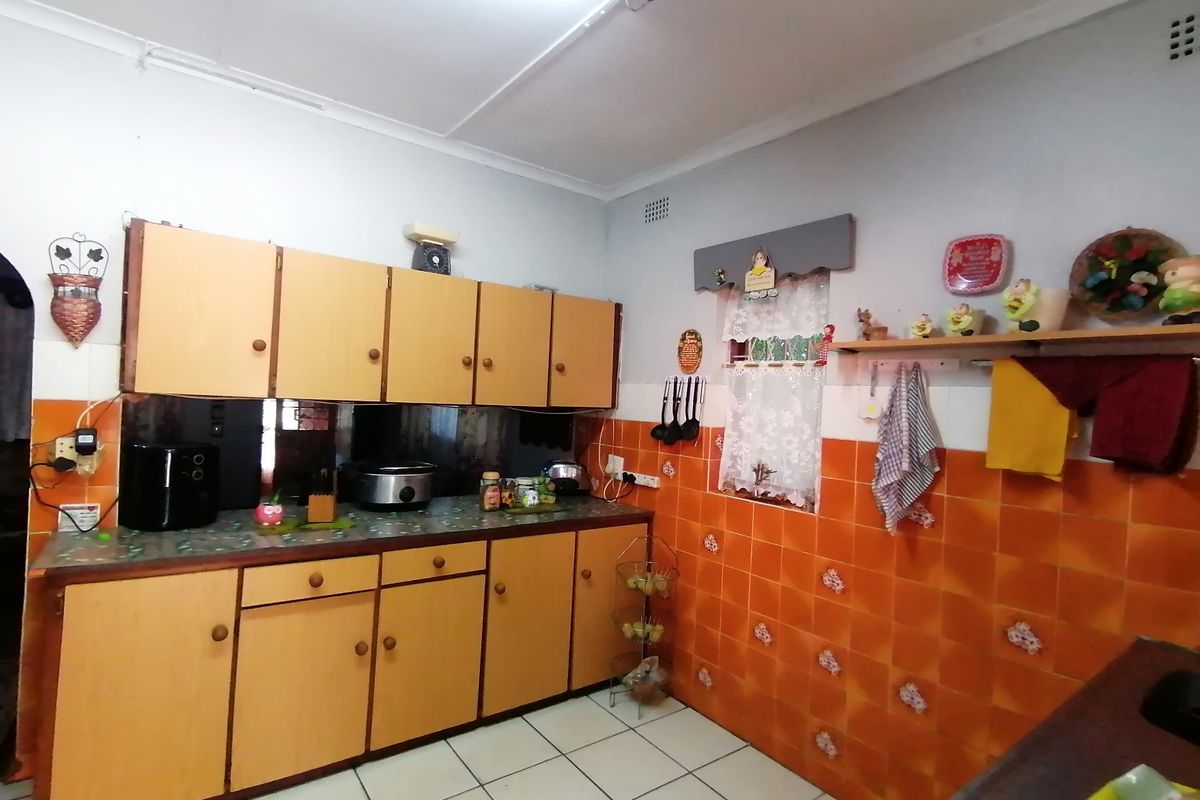 A dated kitchen featuring wooden cabinetry, orange wall tiles, and tiled flooring, offering a functional layout ready for modern renovation and updates.