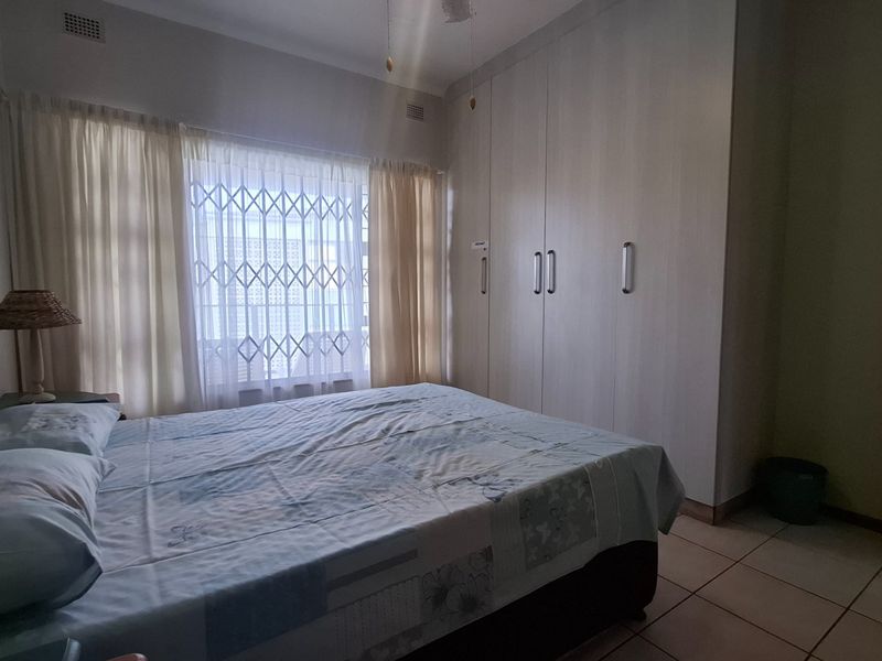 A bedroom featuring built-in cupboards, tiled flooring, and a security gate on the window.