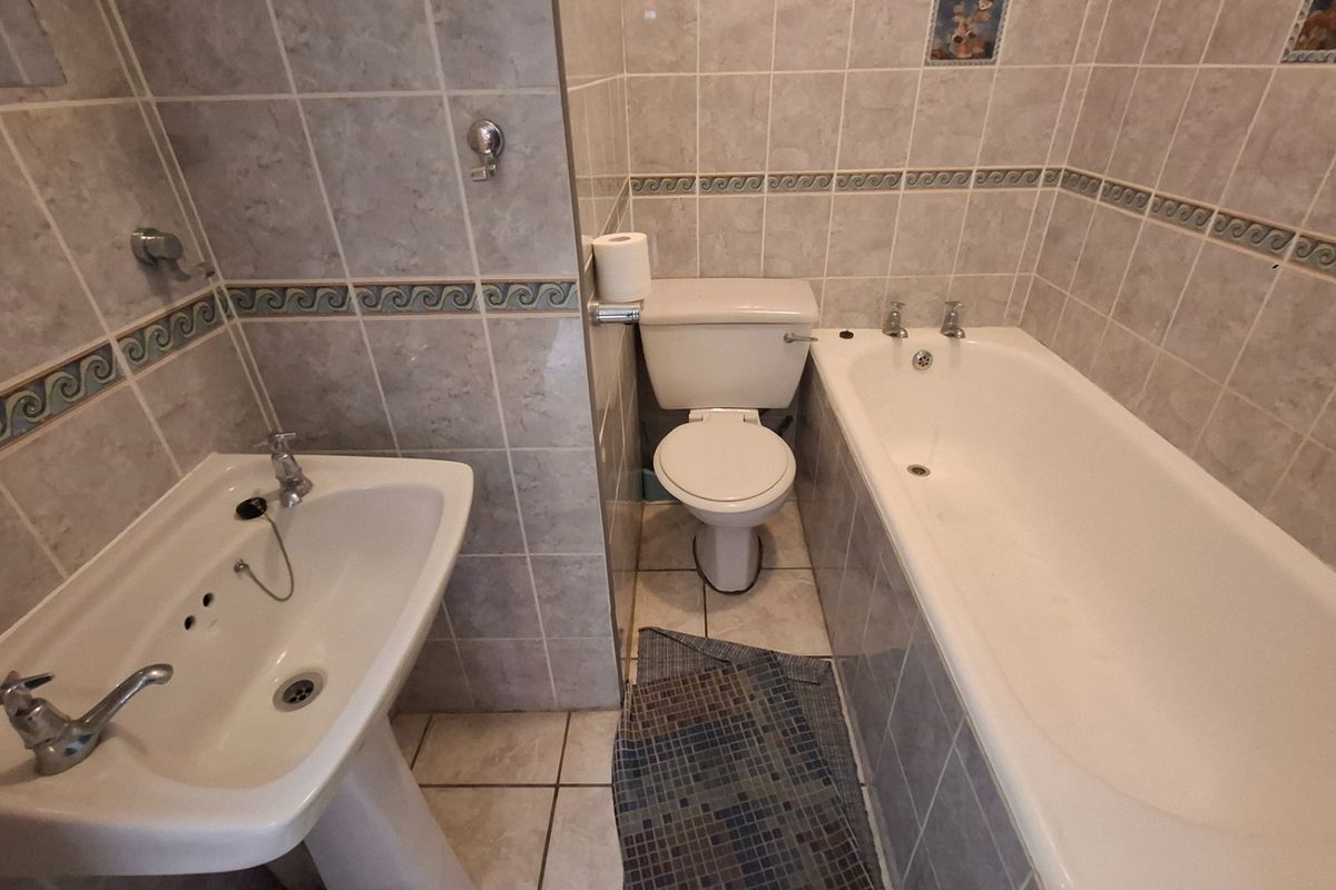 A functional bathroom featuring a pedestal basin, a standard bathtub with chrome taps, and a toilet, finished with neutral wall and floor tiling.