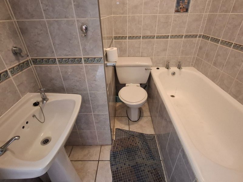 A functional bathroom featuring a pedestal basin, a standard bathtub with chrome taps, and a toilet, finished with neutral wall and floor tiling.
