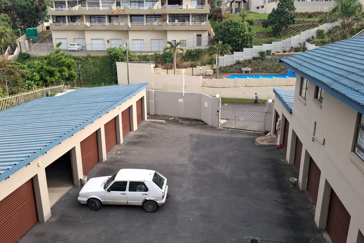 An elevated view of the apartment complex parking area featuring multiple garage units with roller doors and a paved driveway.