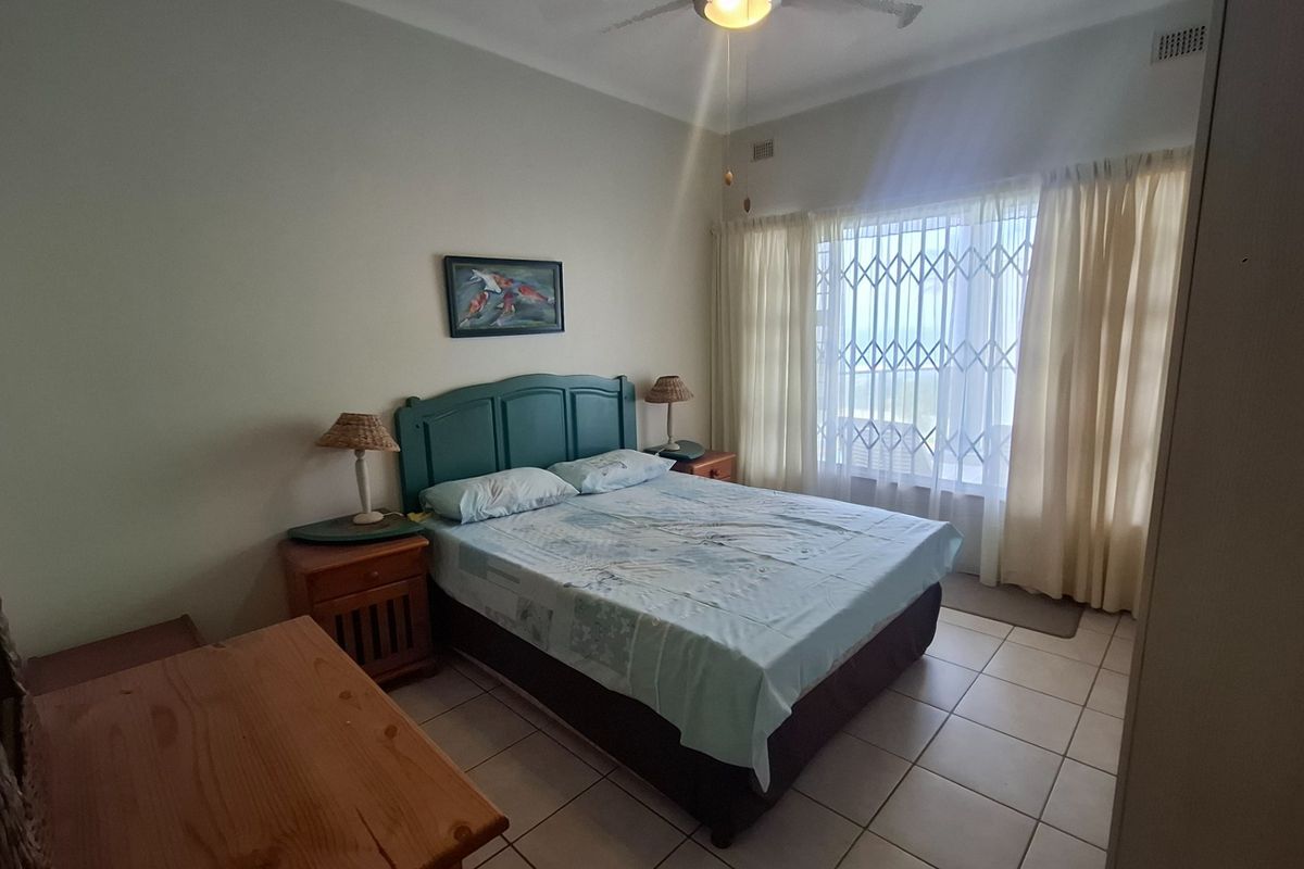 A functional bedroom featuring tiled flooring, a ceiling fan, and a security gate on the window, providing a practical and secure living space.