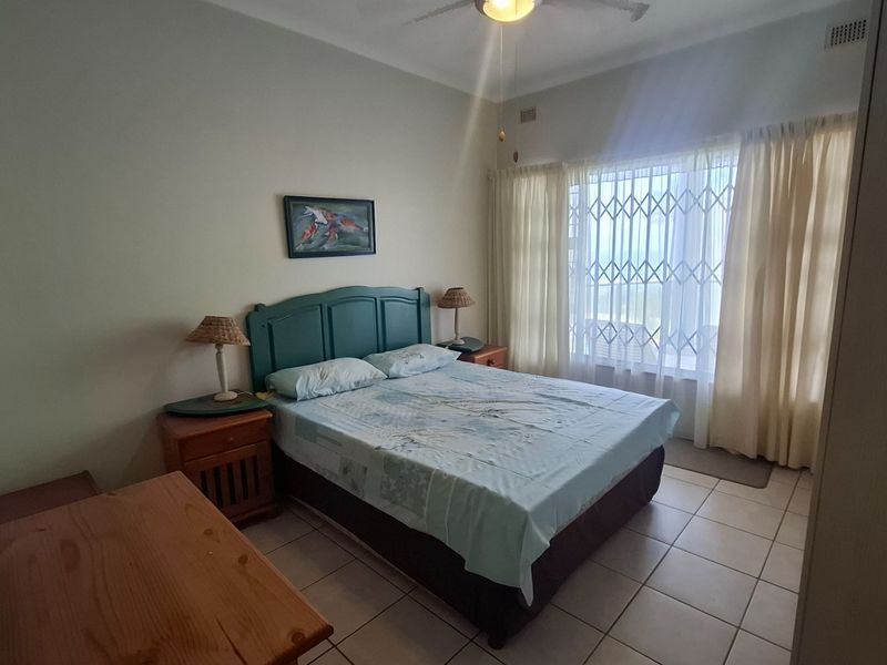 A functional bedroom featuring tiled flooring, a ceiling fan, and a security gate on the window, providing a practical and secure living space.
