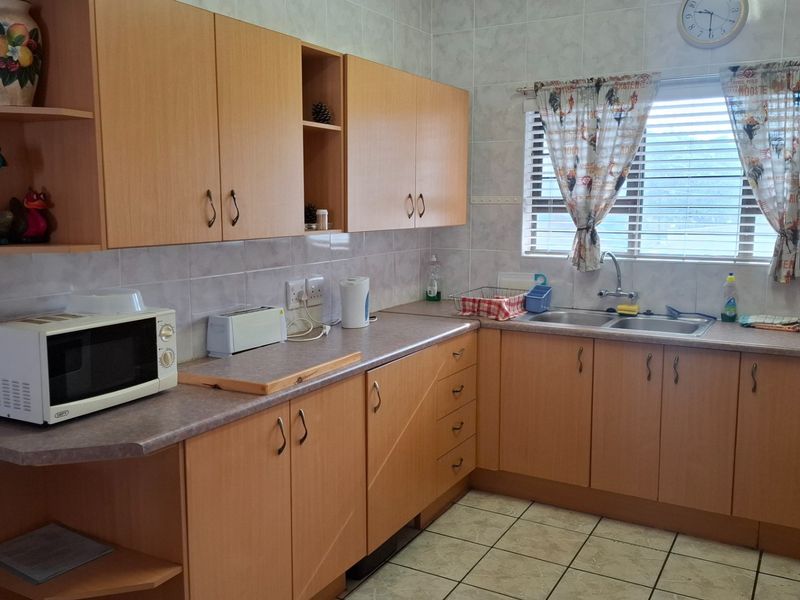 A functional kitchen featuring light wood-finish cabinetry, tiled splashbacks, double stainless steel sink, and tiled flooring.