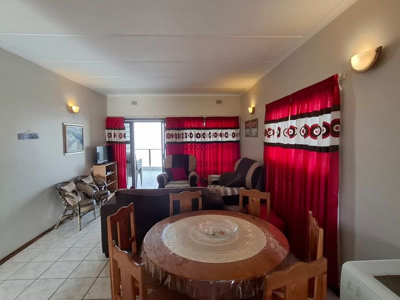 Open plan living and dining area featuring tiled flooring, wall-mounted lighting, and direct access to an outdoor balcony through sliding glass doors.