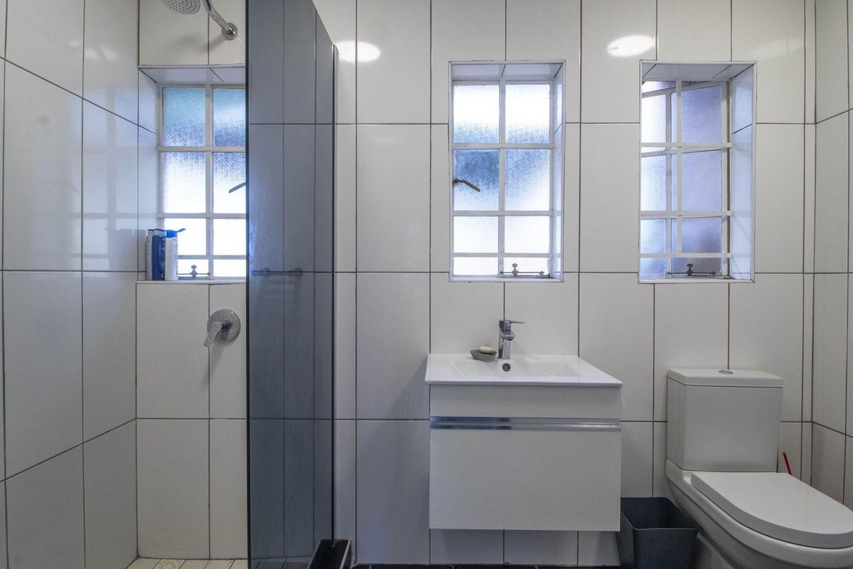 A clean, modern bathroom featuring white wall tiles, a wall-mounted vanity with a basin, a glass shower screen, and a standard toilet.