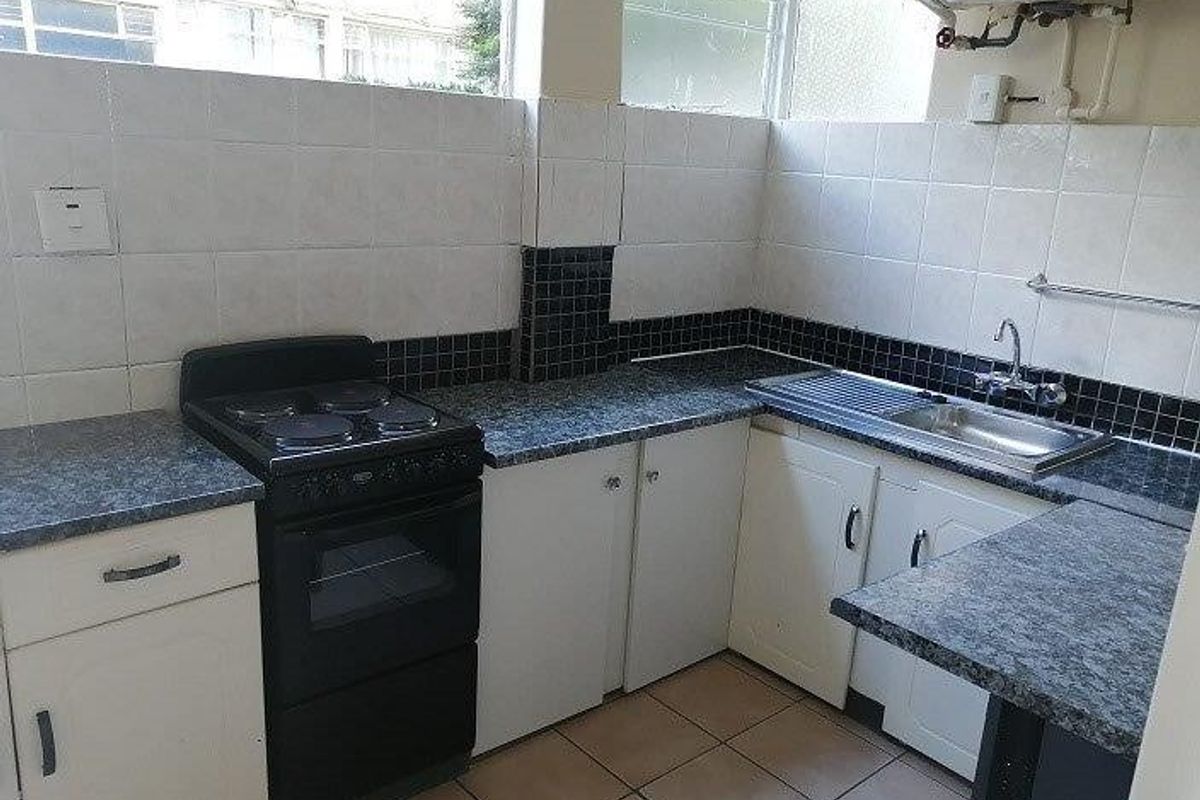 A functional kitchen featuring laminate countertops, a freestanding electric stove, tiled splashbacks, and a stainless steel sink with exposed plumbing.