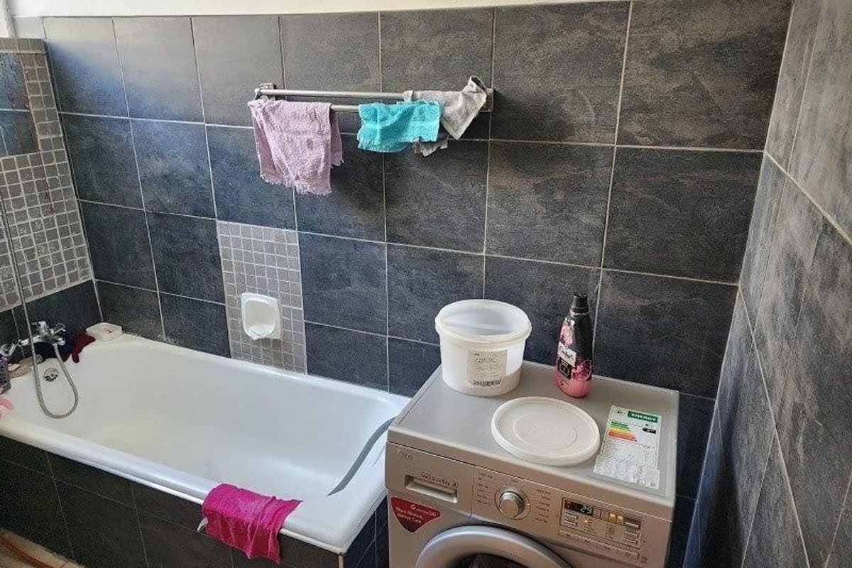 A functional bathroom featuring a built-in bathtub with dark tiled surround and integrated laundry space with washing machine connection.