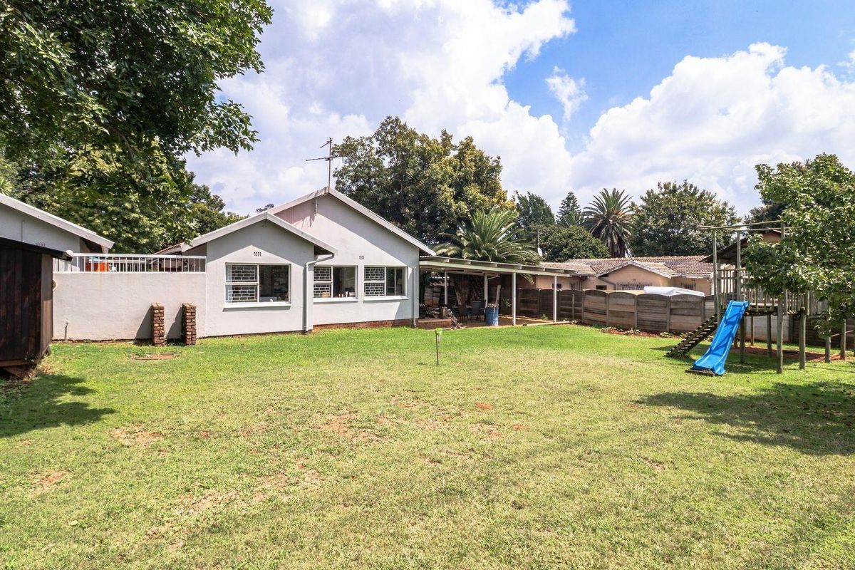 Spacious rear garden featuring a large lawn, covered patio area, and established trees, providing a private outdoor space for relaxation and recreation.