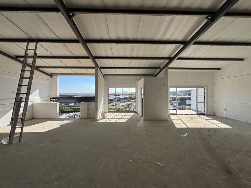 Spacious open-plan industrial interior featuring exposed steel roof trusses, concrete flooring, and large windows offering natural light and expansive views.