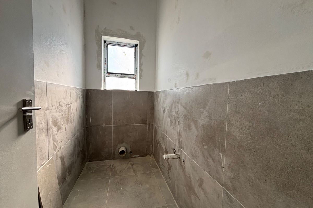 An unfinished bathroom space featuring tiled flooring and partial wall tiling, currently awaiting the installation of sanitary fixtures and final wall finishing.