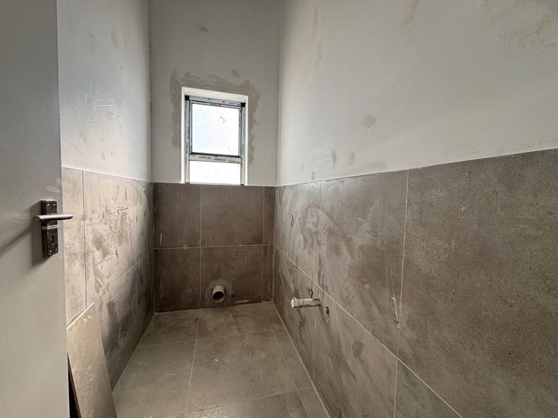 An unfinished bathroom space featuring tiled flooring and partial wall tiling, currently awaiting the installation of sanitary fixtures and final wall finishing.
