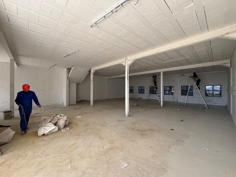 A large, open-plan industrial utility space featuring exposed steel columns, concrete block ceilings, and multiple windows, currently undergoing maintenance and finishing work.