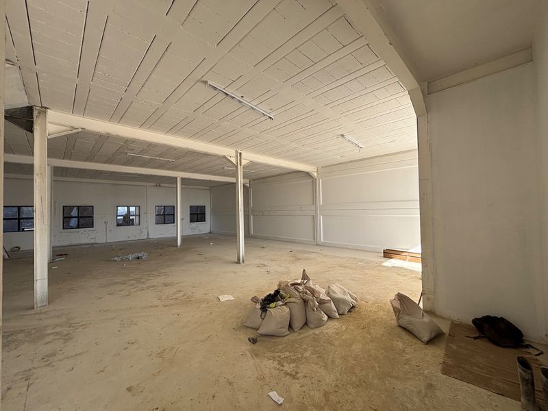 Spacious industrial utility area featuring exposed concrete ceilings, steel support columns, and large windows, offering a versatile open-plan layout for various commercial uses.