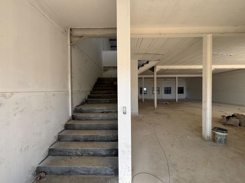 An open-plan industrial utility space featuring a concrete staircase, exposed structural columns, and unfinished surfaces, suitable for warehouse or workshop conversion.
