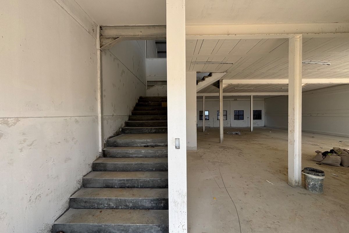 An open-plan industrial utility space featuring a concrete staircase, exposed structural columns, and unfinished surfaces, suitable for warehouse or workshop conversion.