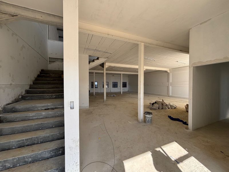 An expansive, unfinished industrial utility space featuring exposed concrete structural elements, a staircase, and open-plan layout suitable for commercial or warehouse development.