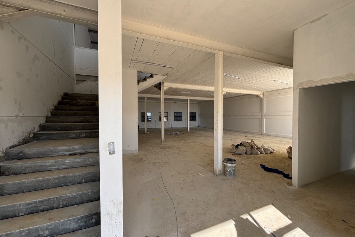 An expansive, unfinished industrial utility space featuring exposed concrete structural elements, a staircase, and open-plan layout suitable for commercial or warehouse development.