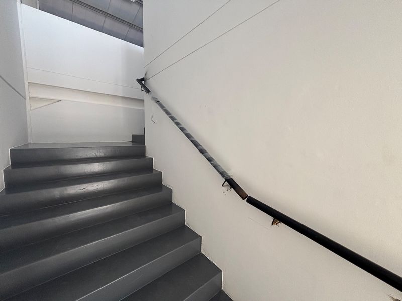 A staircase in an industrial setting featuring a broken handrail and damaged wall mounting, requiring immediate repair for safety.